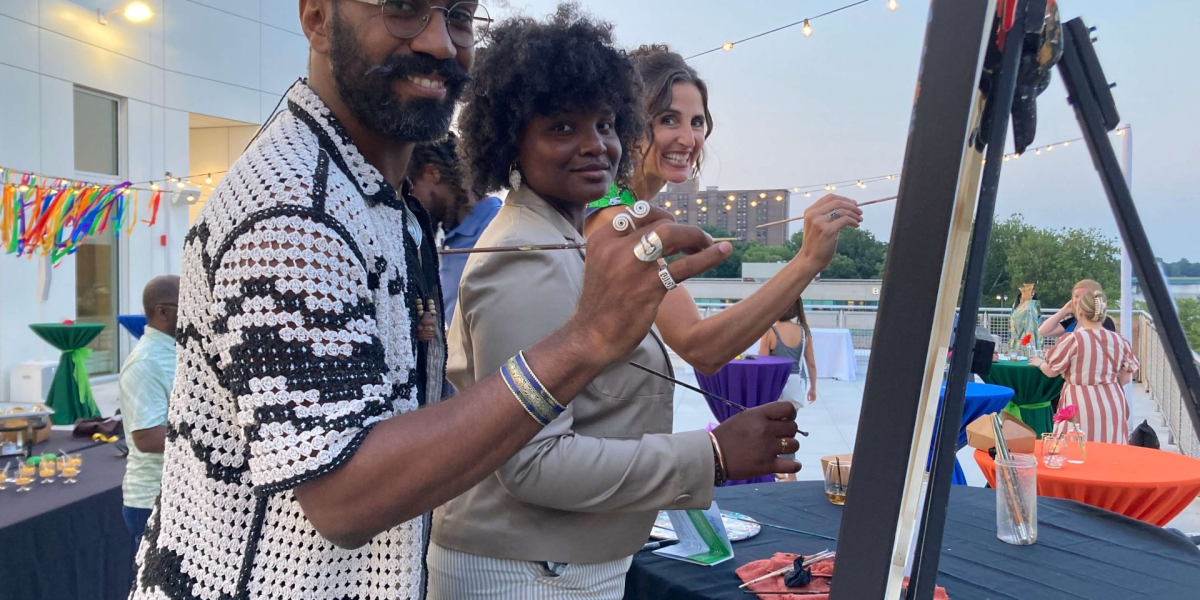 Three adults painting together at an outdoor event